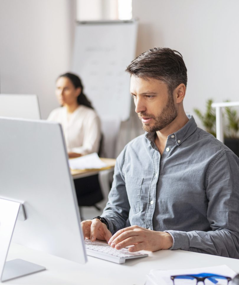 Busy handsome millennial european man manager typing at computer at workplace in modern office interior, copy space. Business, finance planning, data analysis, developing in company and project work